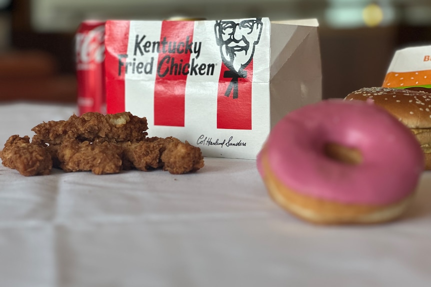 A handful of KFC chicken pieces next to a pink iced donut.