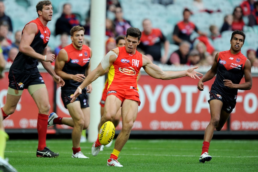 A man playing AFL football prepares to kick the ball. 