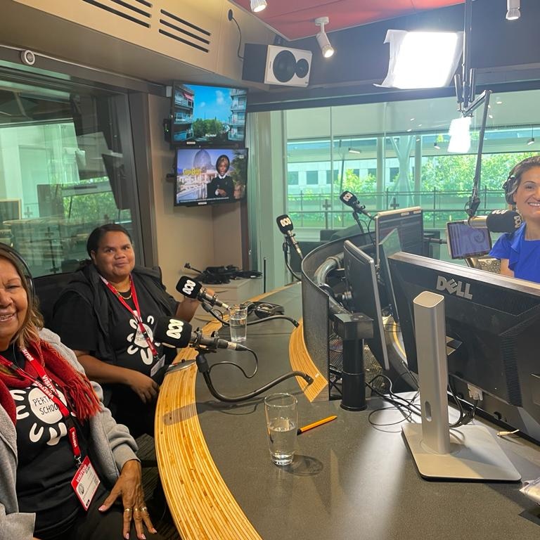three women in a radio studio smile at the camera from behind their microphones