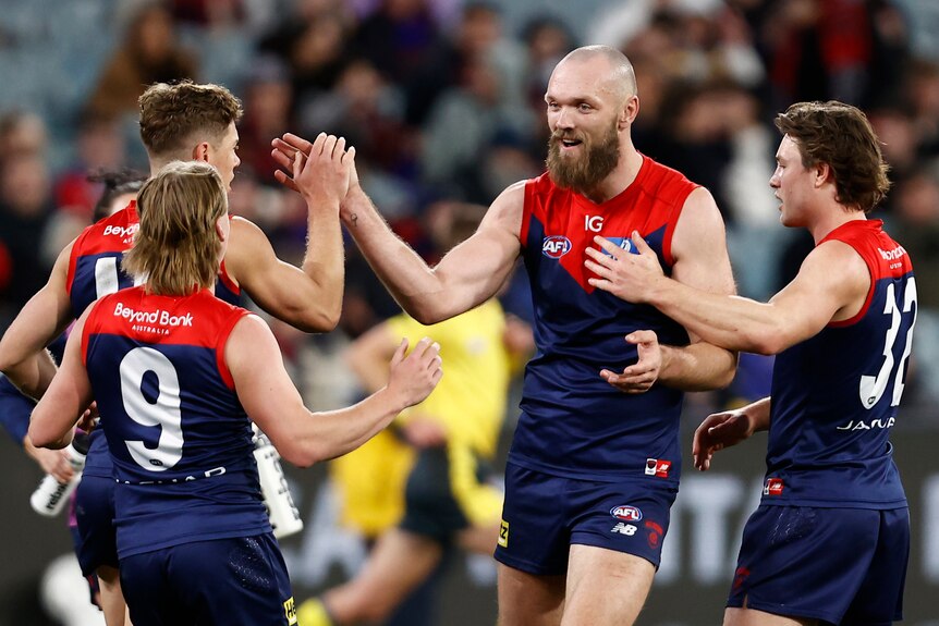 A Melbourne AFL captain smiles and high-fives teammates as they gather to celebrate a goal.
