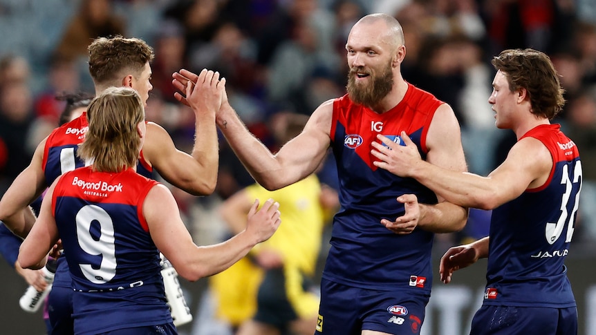 A Melbourne AFL captain smiles and high-fives teammates as they gather to celebrate a goal.