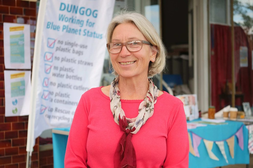 Woman in glasses with blonde bob wearing a salmon pink shirt.