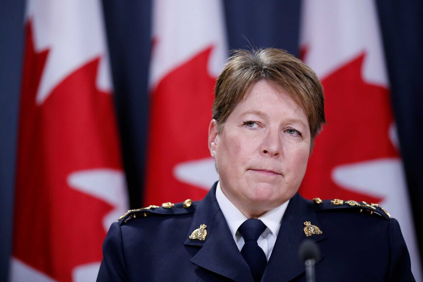 Brenda Lucki stands at a microphone in front of a Canadian flag, wearing a formal police uniform.