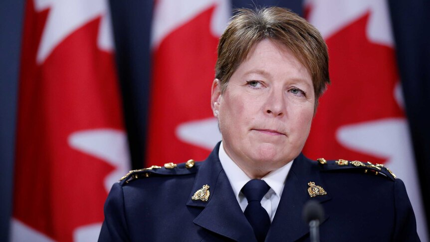 Brenda Lucki stands at a microphone in front of a Canadian flag, wearing a formal police uniform.