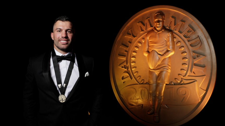A man poses in front of a statue of the Dally M medal