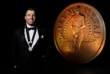 A man poses in front of a statue of the Dally M medal