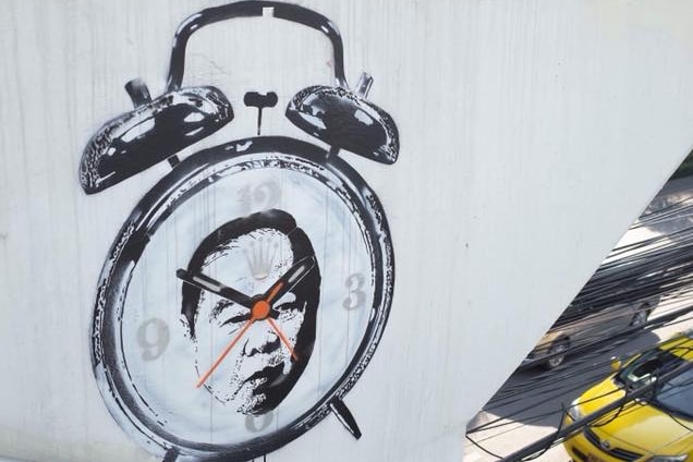 A picture of a Rolex logo alarm clock with Thailand's deputy Prime Minister General Prawit Wongsuwan on a white wall.