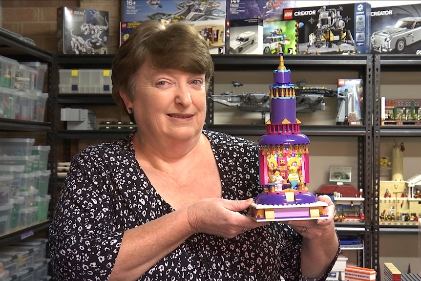 Woman looks to camera holding a Lego model of the TV show "I dream of Jeannie".