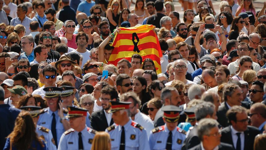In a crowd of tightly packed people, one person holds up the red and yellow Catalan flag.
