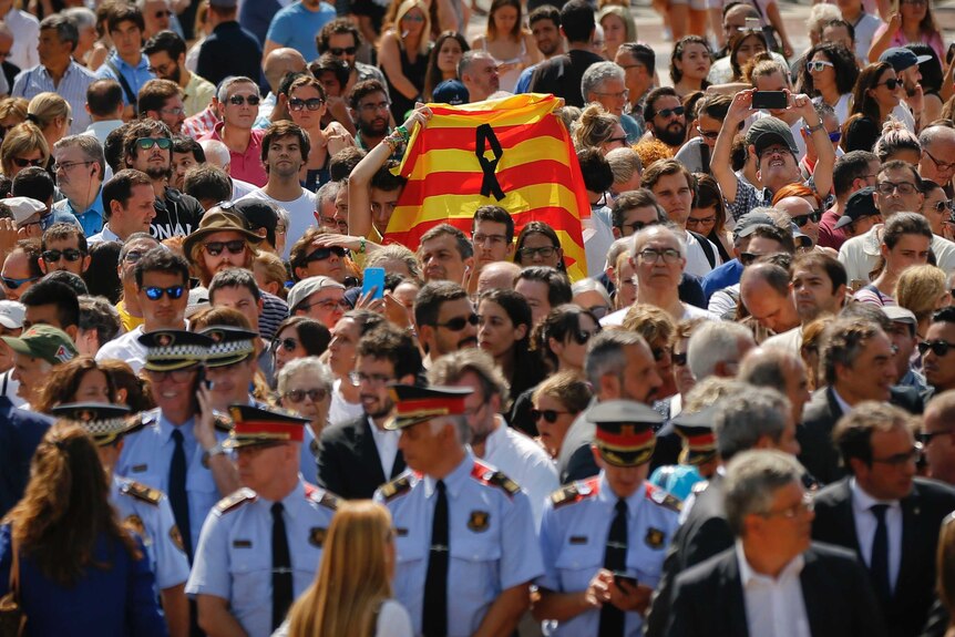 In a crowd of tightly packed people, one person holds up the red and yellow Catalan flag.