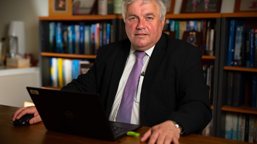 Rex Patrick sitting at a desk, wearing a suit and purple tie, with a laptop in front of him.