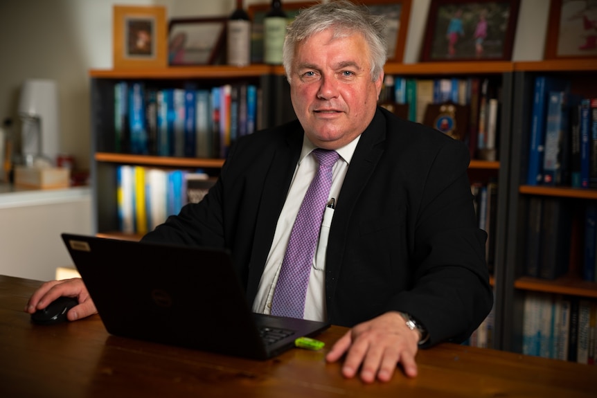 Rex Patrick sitting at a desk, wearing a suit and purple tie, with a laptop in front of him.