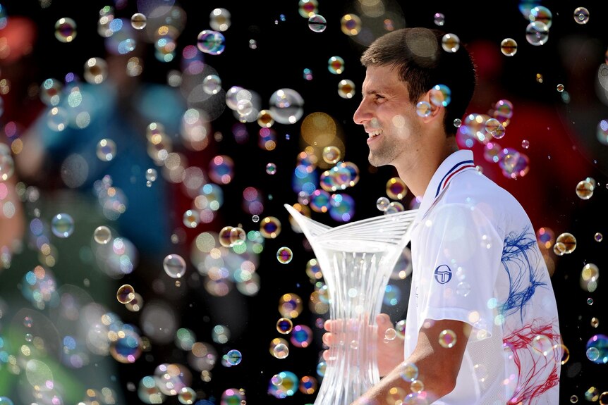 Novak Djokovic holds the winner's trophy and watches the bubbles after winning in Key Biscayne.