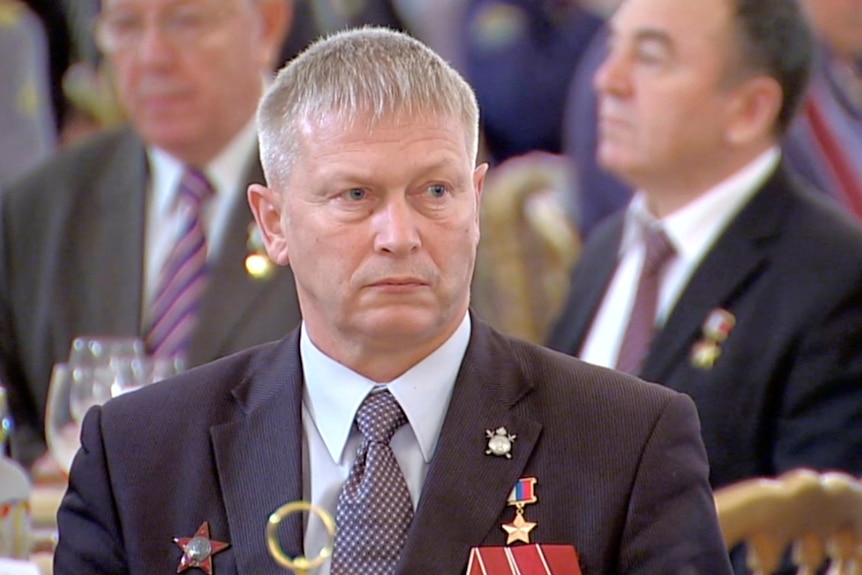 Andrei Troshev sits at a dinner table, wearing military medals on his suit jacket