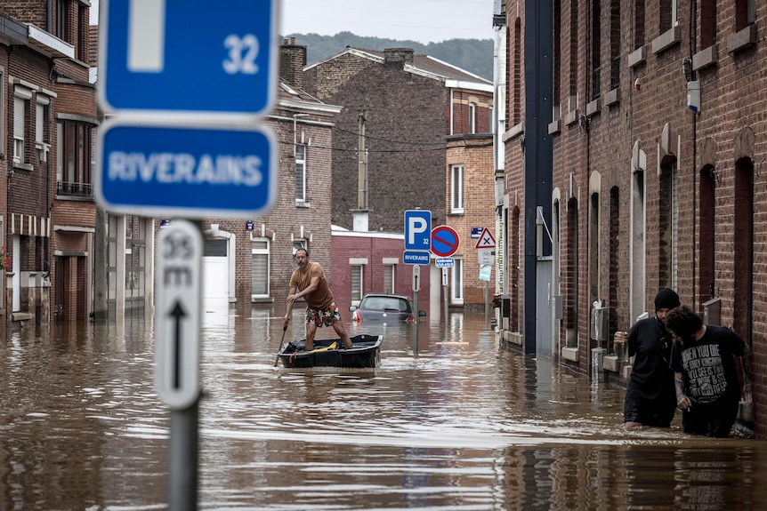A man stands up rowing a small boat through a flooded street in Liege, Belgium.
