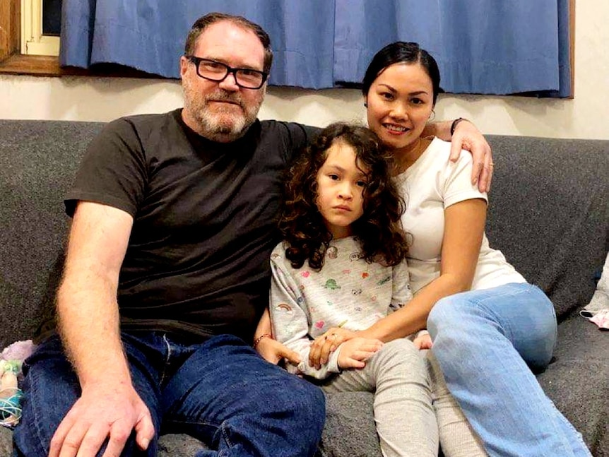 A mum and a dad sit with their daughter on a couch.