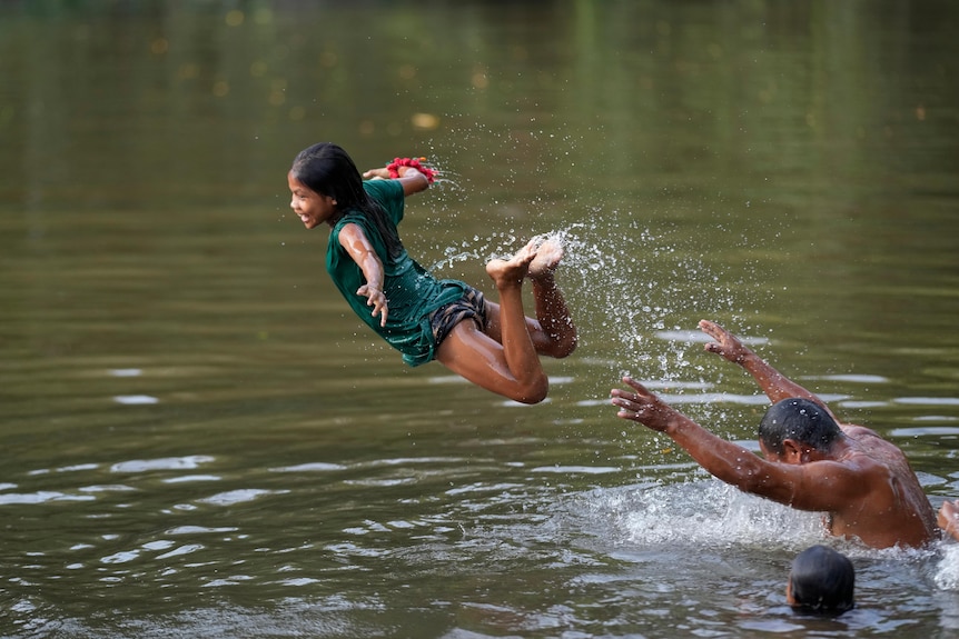 A young, laughing girl is mid-air as she plays in the river with a man, another child's head can be seen in the water