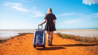 A woman pulling a blue suitcase down a red dirt country path.