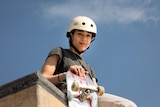 A young woman looks down from atop a skate park bowl.