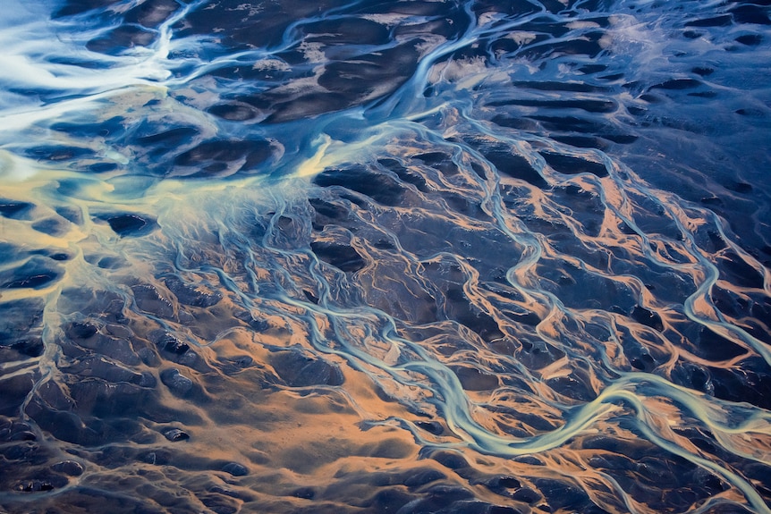 Aerial shot of a frozen body of water in Iceland. The patterns look like sprawling tentacles of cool white, blue and soft pink.