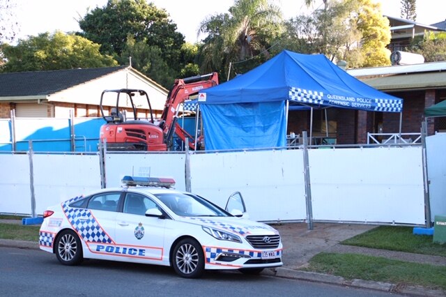 A police car sits outside a property where a temporary fence has been erected to prevent an investigation being viewed