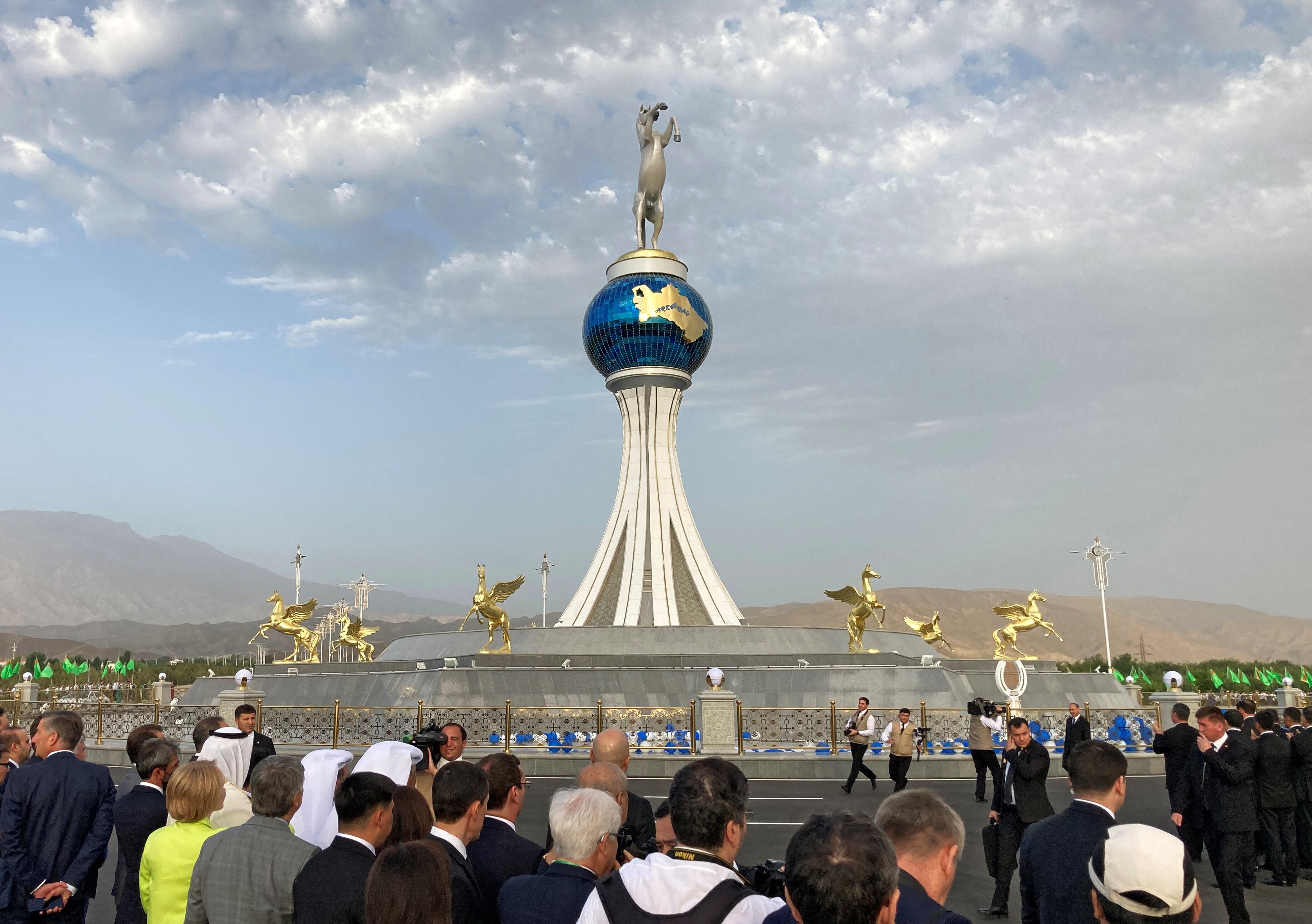 A statue of a rearing silver horse is atop a blue globe with a golden image of Turkmenistan that sits on large pillars.