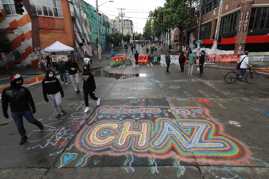 People walking down a barricaded street with 'Welcome To Chaz' written in chalk on the ground