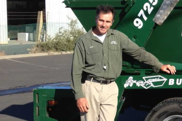 A man leans on a garbage truck.