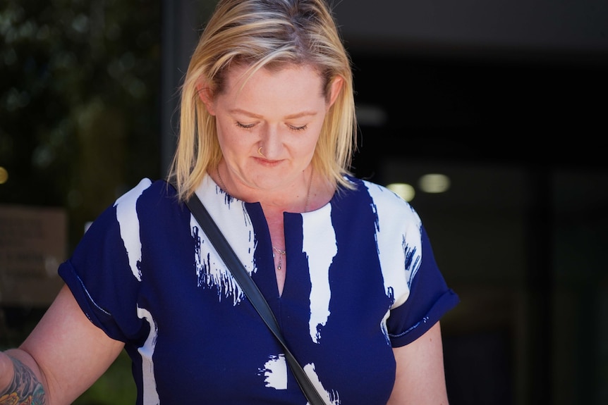 A medium close-up of a blonde white woman, looking down. She is going down some steps.