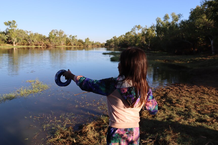 una joven aborigen pescando junto a un río usando un hilo de pescar de mano