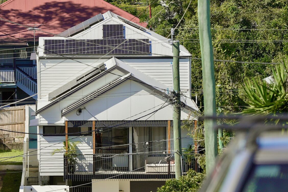 A two-storey house with solar panels on the roof. Lots of powerlines running through the foreground.