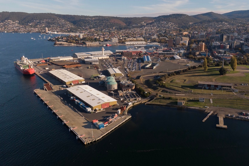 Port area of a city with buildings, green space in the foreground and hills in the background