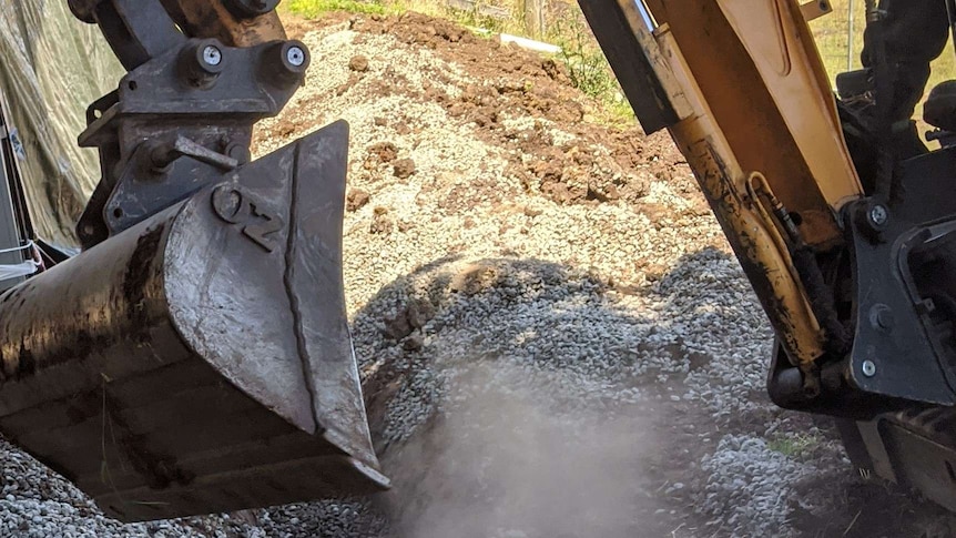 Grader shovel digging in dirt and rocks.