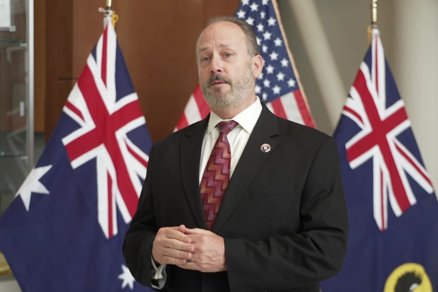 A man in a suit and tie in front of flags.