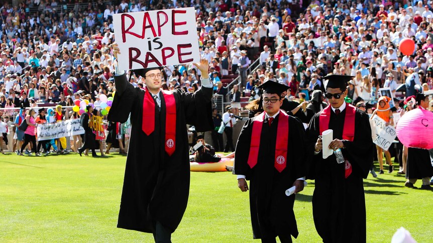 Graduate carries sign that reads: Rape is rape.