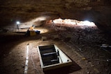 An archaeologist works inside Boodie Cave with tripods and sampling equipment.