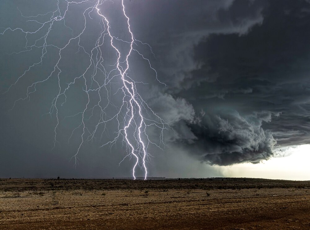 Lightning across the sky with a black cloudy background dry paddocks into the distance