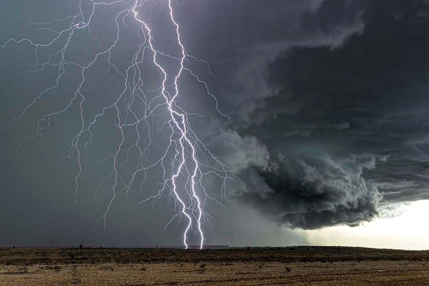 Lightning across the sky with a black cloudy background dry paddocks into the distance