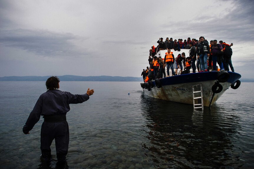 A Greek man talks to asylum seekers arriving by boat.
