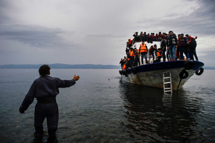 A Greek man talks to asylum seekers arriving by boat.