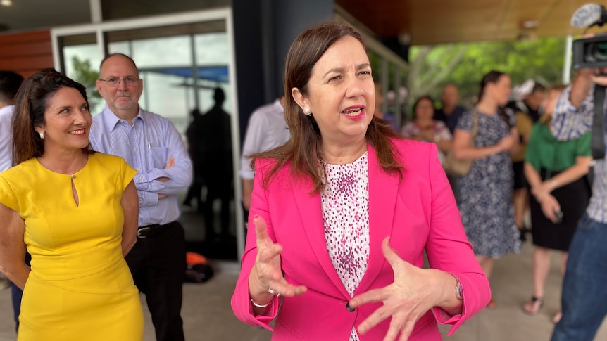 Queensland Premier Annastacia Palaszczuk wears a bright pink jacket and gestures with her hands, smiling. 