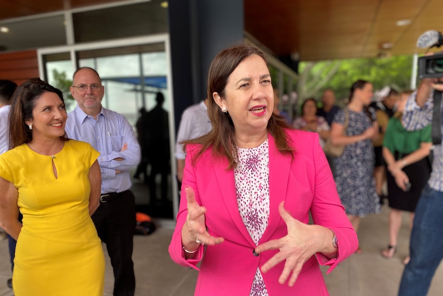 Queensland Premier Annastacia Palaszczuk wears a bright pink jacket and gestures with her hands, smiling. 