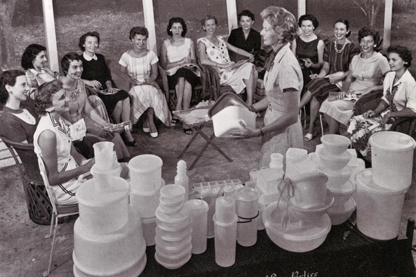 A black and white image showing 50s women at a Tupperware party. In the foreground is a table of Tupperware.