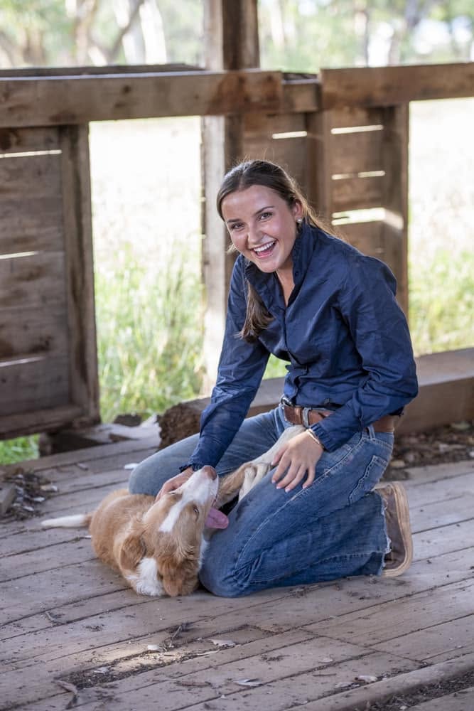 a young woman pats a dog and smiles to the camera