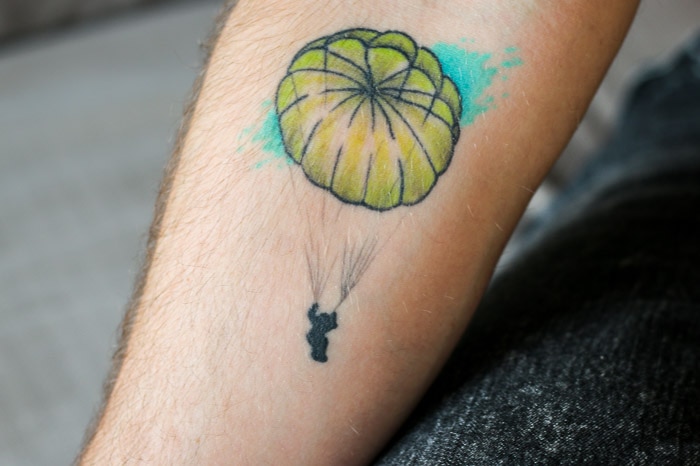 A tattoo of a person falling with a parachute on a man's arm.