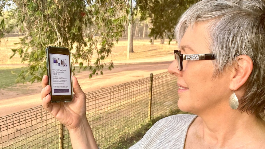 Amanda Salisbury looks at an iPhone with the COVIDSafe app displayed on the screen
