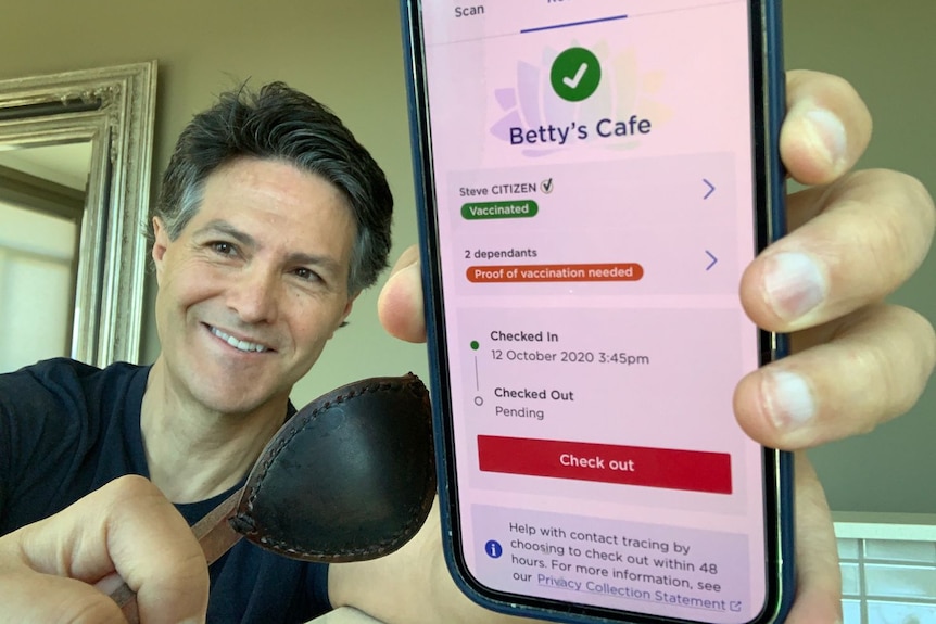 A man holds a phone that reads 'COVID-Safe check-in' and 'Betty's cafe'
