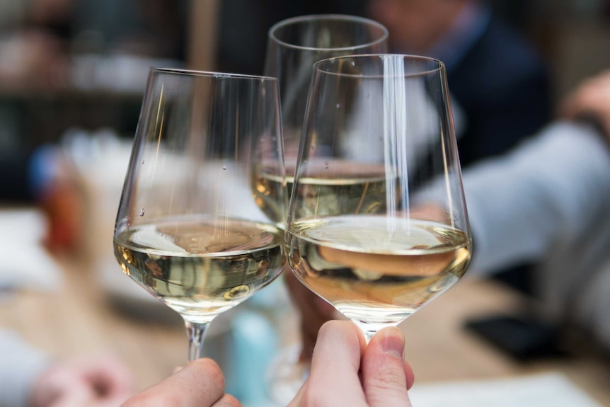 Three wine glasses, filled with white wine, pressed together in a toast.