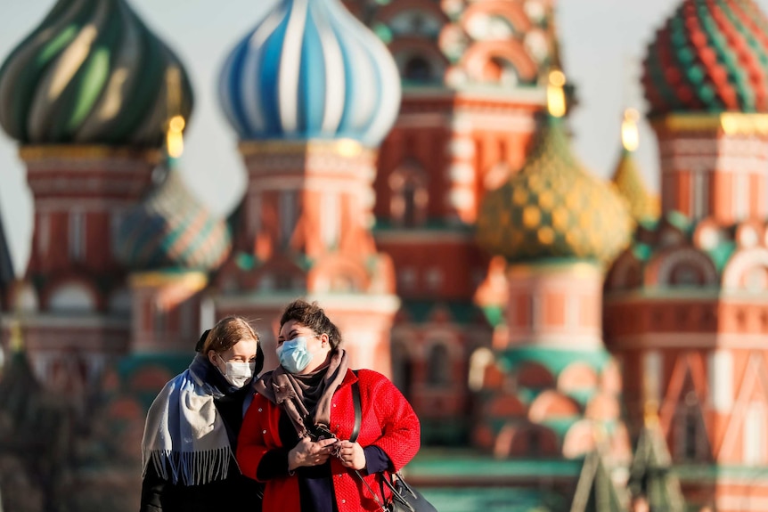 Two women in surgical masks laughing together in front of St Basil's Cathedral in Russia
