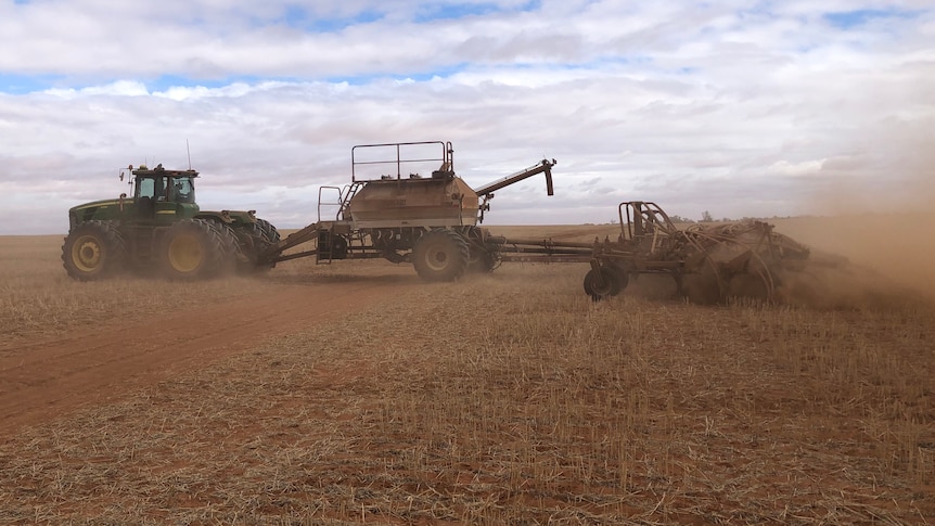 A tractor moves through a dry and dusty paddock sowing barley